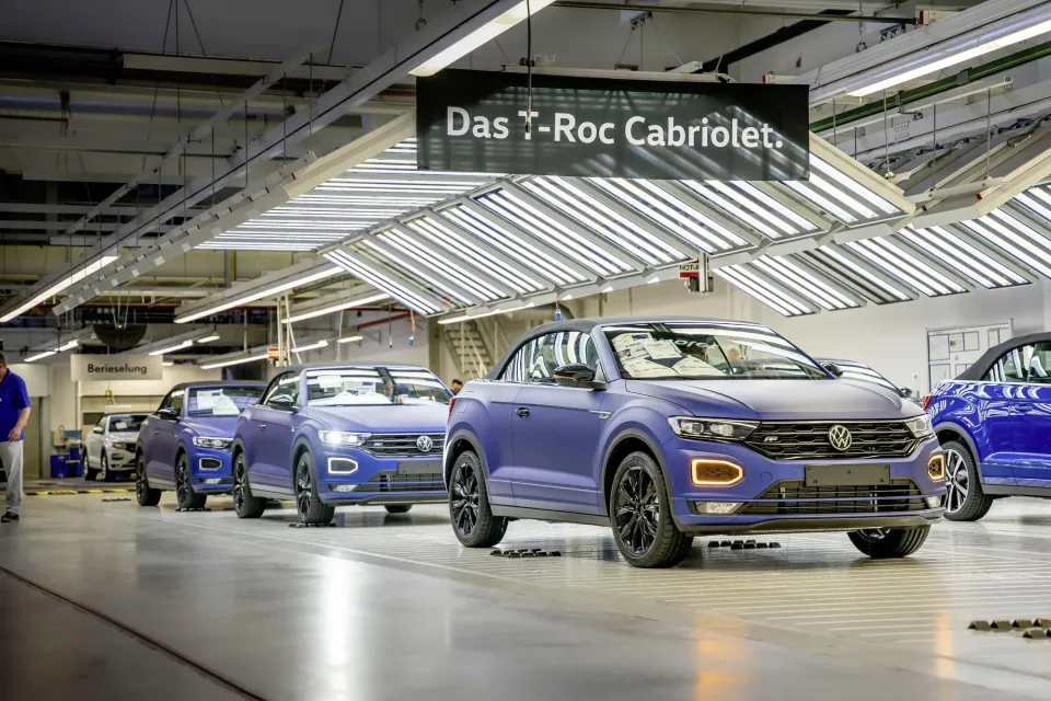 Volkswagen T-Roc Cabriolet convertibles lined up on a factory production line, with a sign overhead reading 'Das T-Roc Cabriolet'