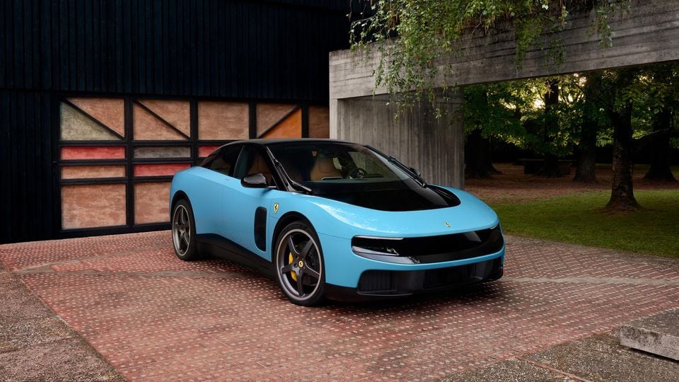 A light blue Ferrari Luce sports car seen from the front-side angle, parked on a brick courtyard in front of a modern building