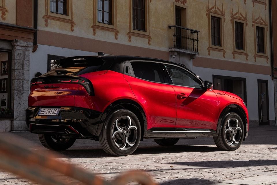 A red Alfa Romeo Junior SUV seen from the rear three-quarter angle, parked on a cobblestone surface in front of a European-style building