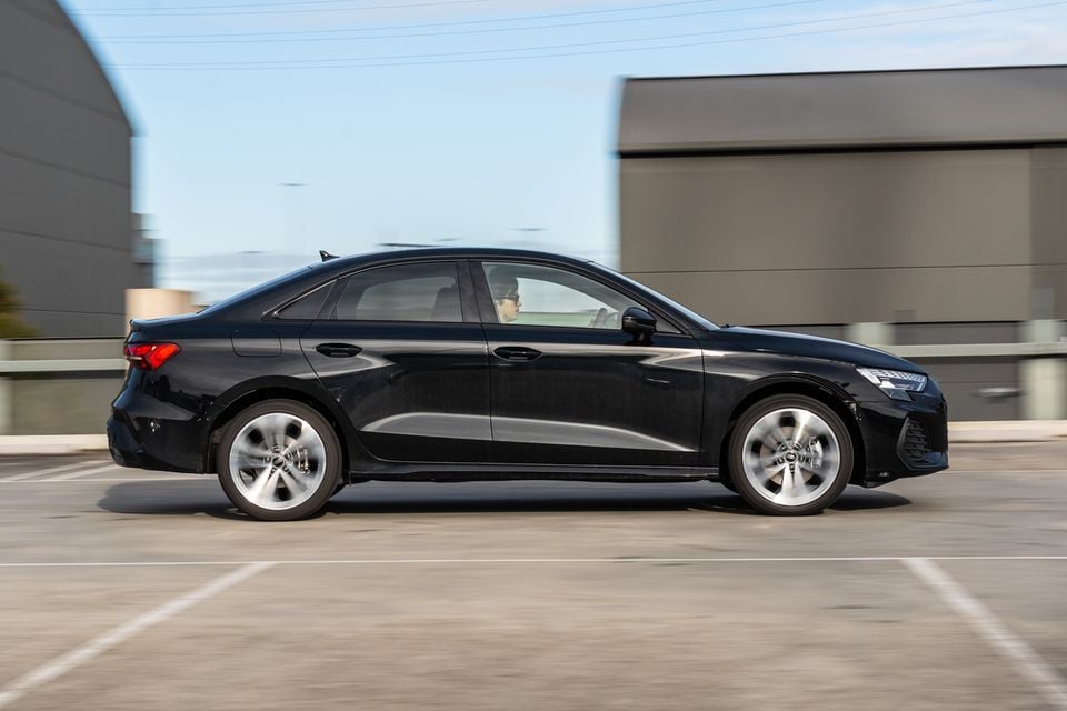 A black 2026 Audi A3 sedan seen from the side while driving through a car park