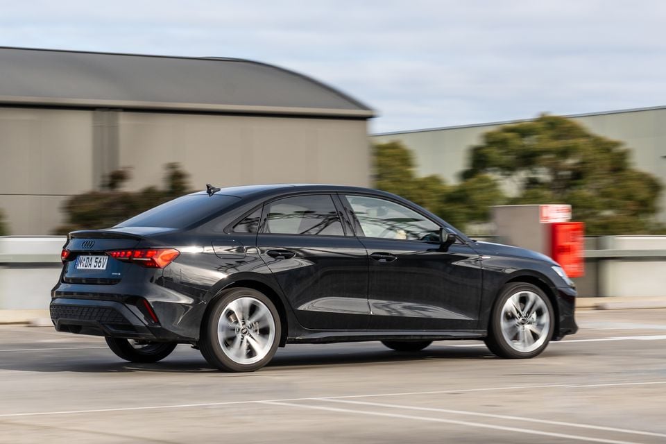 A black 2026 Audi A3 sedan seen from the rear three-quarter angle while driving through a car park