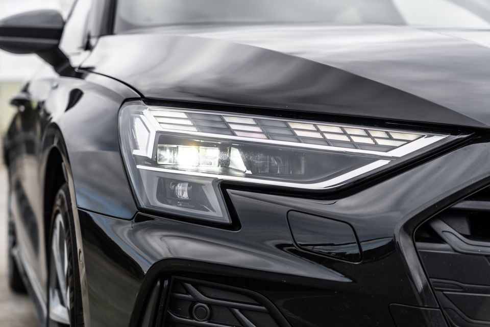 Close-up of the LED headlight on a black 2026 Audi A3 sedan, showing sharp angular styling and illuminated light elements