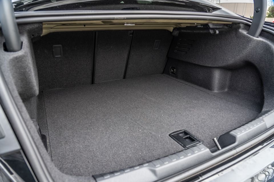The empty, carpeted boot of a 2026 Audi A3 sedan, viewed from the rear with the lid open, showing fold-down rear seat access levers and a flat load floor.