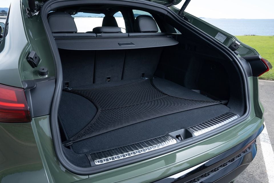 Boot space of a green 2026 Audi Q5 e hybrid Sportback SUV, open from the rear showing a large carpeted cargo area with a cargo net and retractable load cover