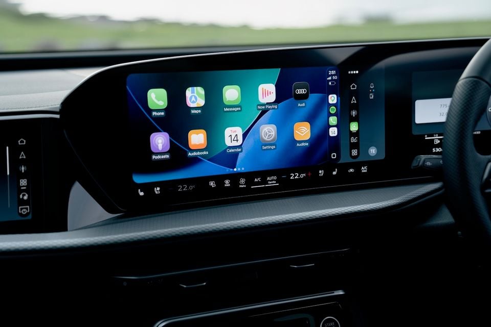 The infotainment touchscreen of an Audi Q5 displaying Apple CarPlay with app icons including Phone, Maps, Messages, Podcasts, and Audiobooks, with climate controls visible below
