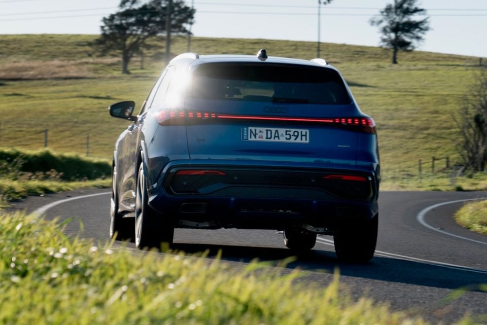 A dark blue 2026 Audi Q5 SUV seen from the rear while driving along a winding rural road in Australia