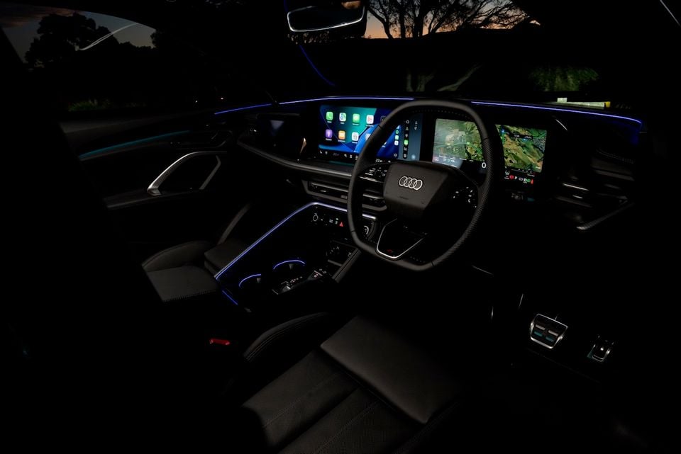 Audi Q5 interior at night showing the dashboard, steering wheel with Audi badge, dual infotainment screens displaying Apple CarPlay and navigation, and blue ambient lighting throughout the cabin