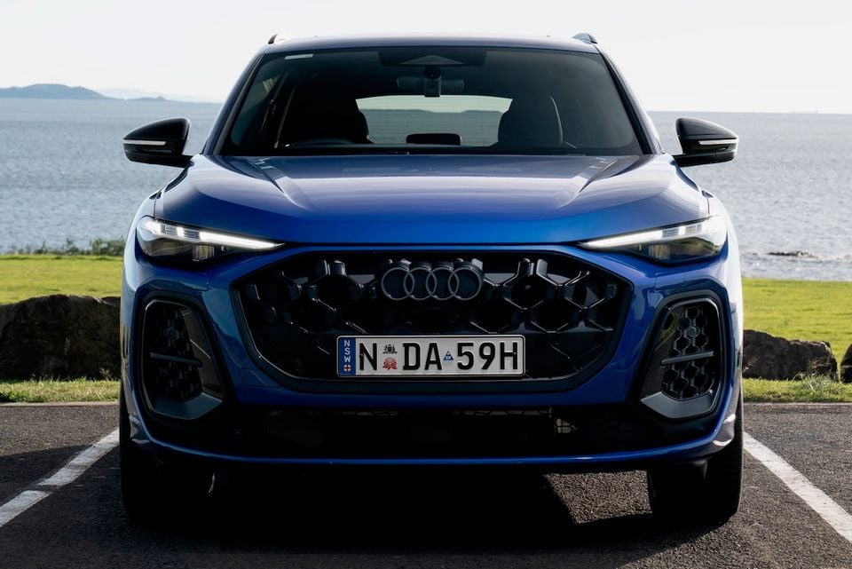 Front view of a blue 2026 Audi Q5 SUV parked near a coastal area with ocean in the background