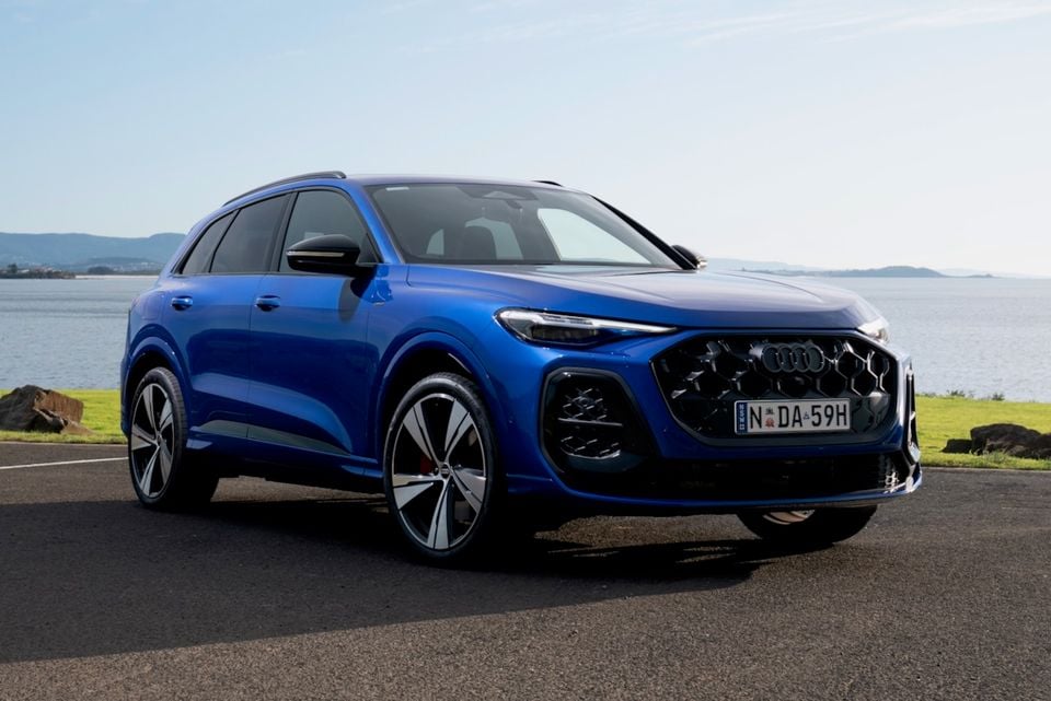 A blue 2026 Audi Q5 SUV seen from the front-side angle, parked near a waterfront on a sunny day.