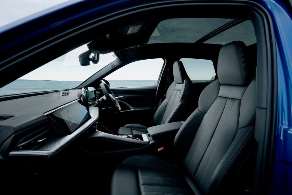 Interior view of a 2026 Audi Q5 showing the front seats, dashboard, large touchscreen infotainment display, and centre console, with a coastal backdrop visible through the windows