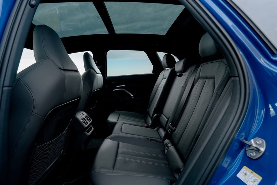 The rear seat interior of a blue 2026 Audi Q5 SUV, showing black leather rear seats, rear air vents, and a panoramic sunroof overhead.