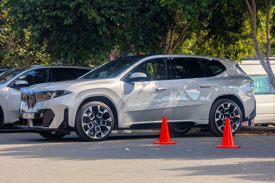 A white BMW iX3 SUV seen from the side, parked with orange traffic cones nearby during a media launch event