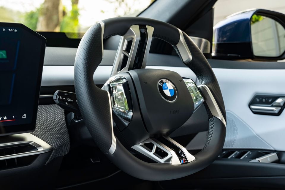 BMW M steering wheel with leather trim and silver accents inside a 2026 BMW iX3, with a touchscreen display visible to the left