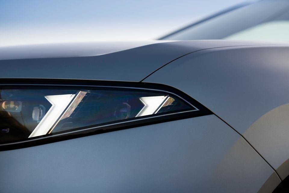Close-up of the LED headlight on a 2026 BMW iX3, showing distinctive arrow-shaped daytime running light signatures on a silver body panel.