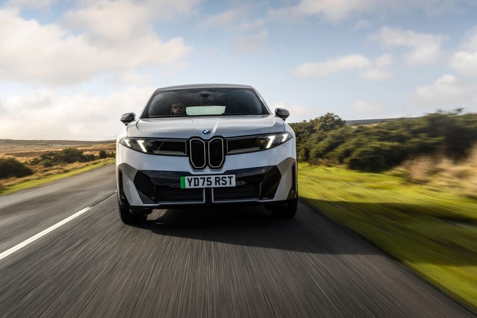 A white BMW iX3 SUV seen from the front while driving on a rural road