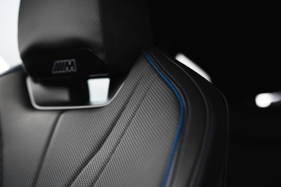 Close-up of a BMW M Sport seat showing perforated leather upholstery with blue stitching detail and the M badge on the headrest, inside a 2026 BMW iX3.