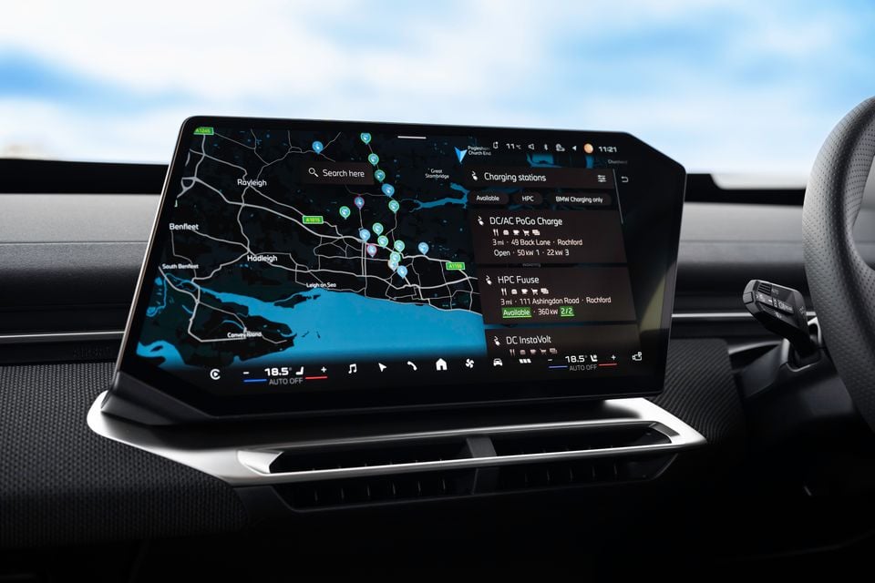 The infotainment touchscreen of a 2026 BMW iX3 displaying a map with nearby EV charging stations listed on the right side panel.