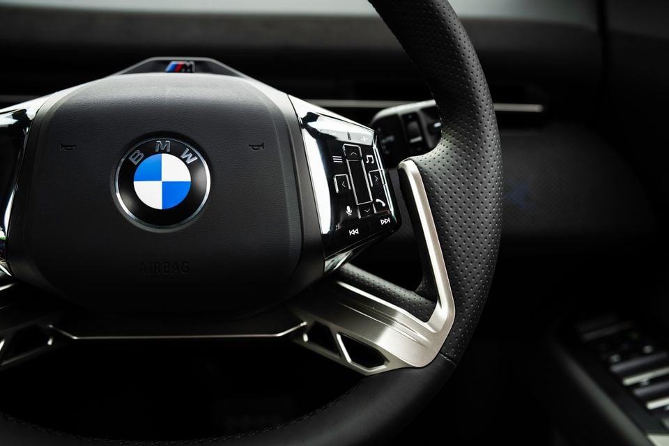 Close-up of the BMW iX3 M Sport Pro steering wheel showing the BMW M logo, perforated leather trim, and multifunction control buttons