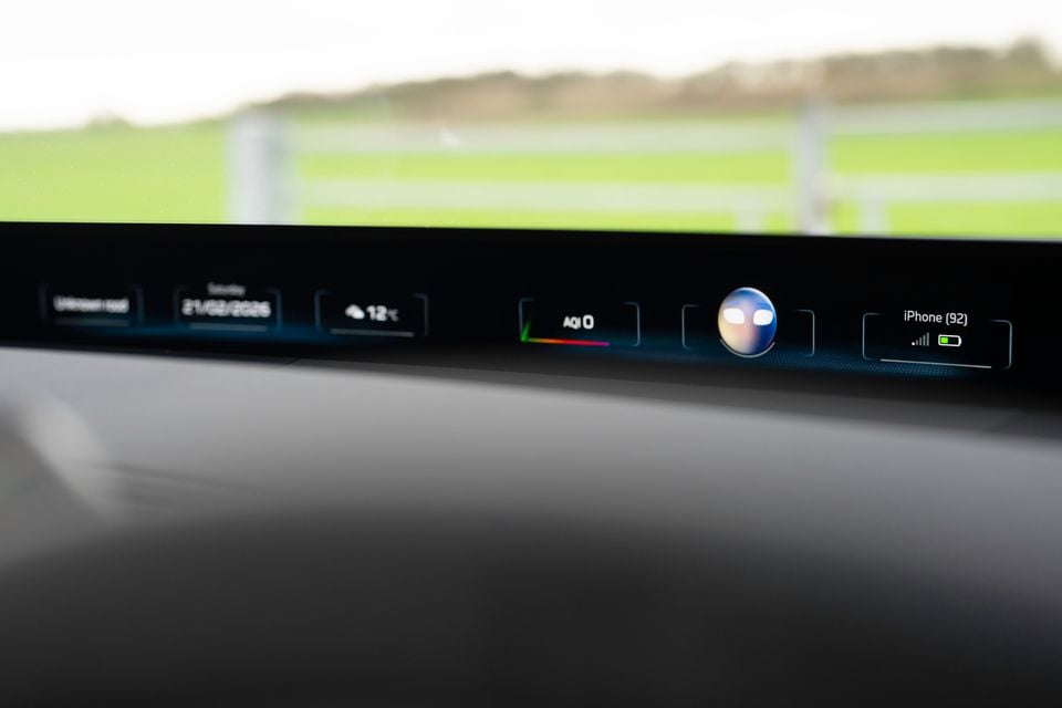 Close-up of the instrument panel display strip in a 2026 BMW iX3 showing date, temperature, air quality index, voice assistant, and connected iPhone status