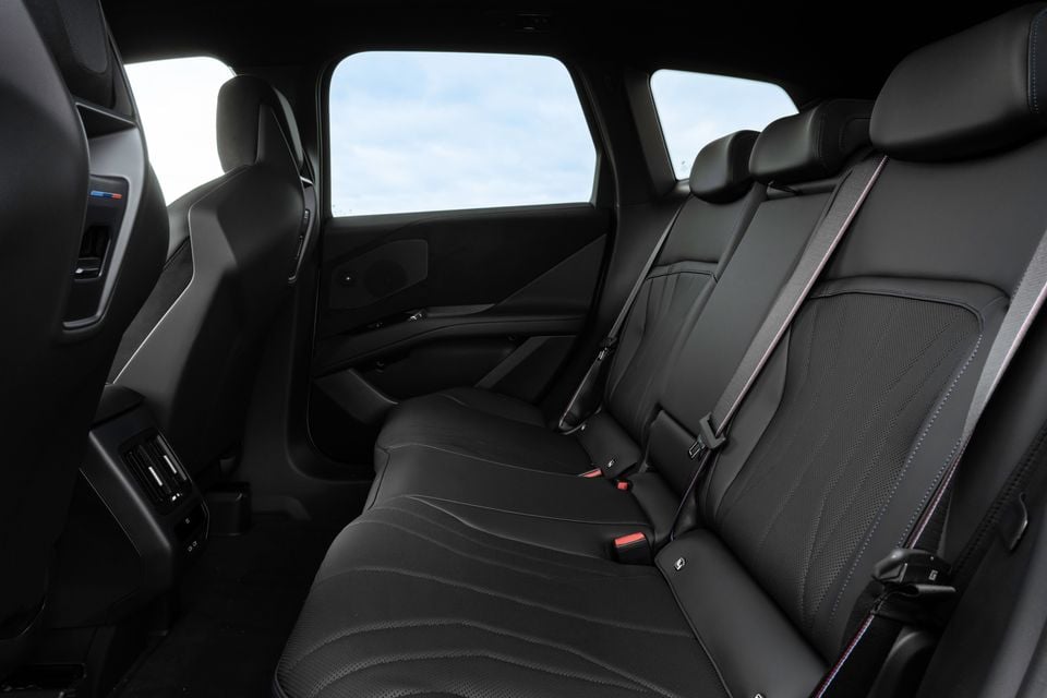 Rear interior of a 2026 BMW iX3 M Sport Pro showing black leather rear seats with seatbelts, rear air vents, and rear door panel