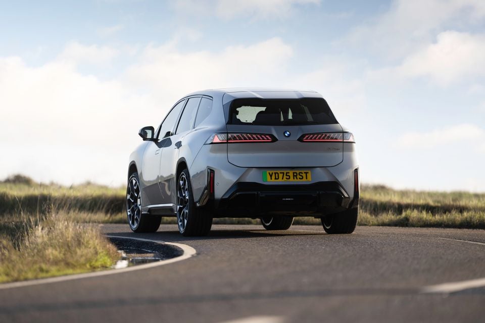 A grey BMW iX3 SUV seen from the rear on a country road