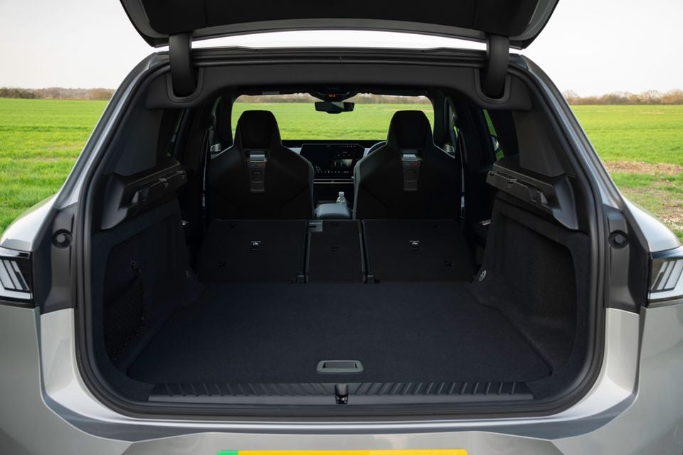 Boot of a 2026 BMW iX3 SUV open with rear seats folded flat, showing a large cargo area, parked in a rural setting