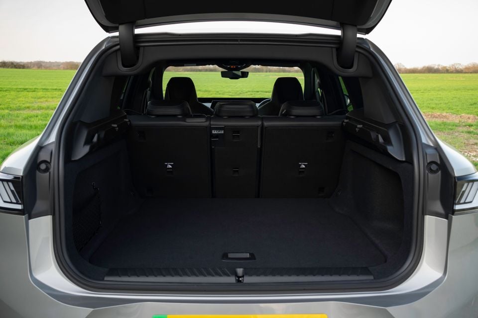 Open boot of a 2026 BMW iX3 SUV showing a large empty cargo area with the tailgate raised, parked in front of a green field