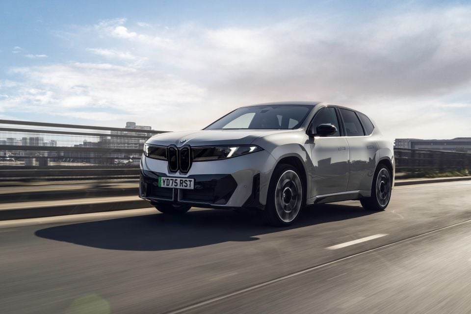 A grey BMW iX3 SUV driving on a highway bridge, seen from the front-left angle