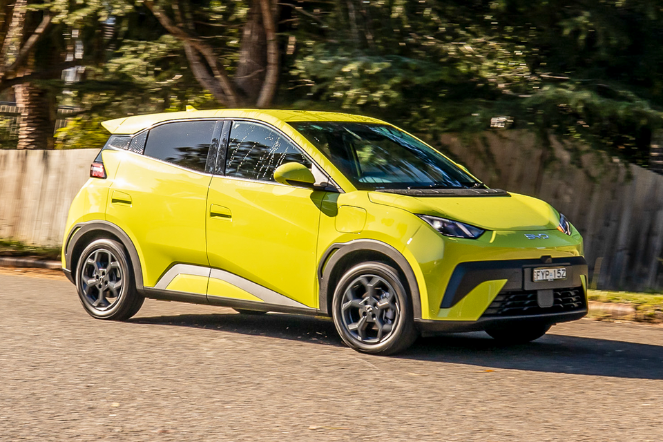 A yellow-green 2026 BYD Atto 1 small SUV driving on a suburban road, seen from the front-side