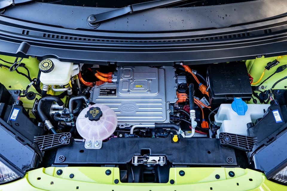 The electric motor bay of a BYD Atto 1 in lime green, showing the BYD-branded power unit with orange high-voltage cables and various fluid reservoirs under an open bonnet.
