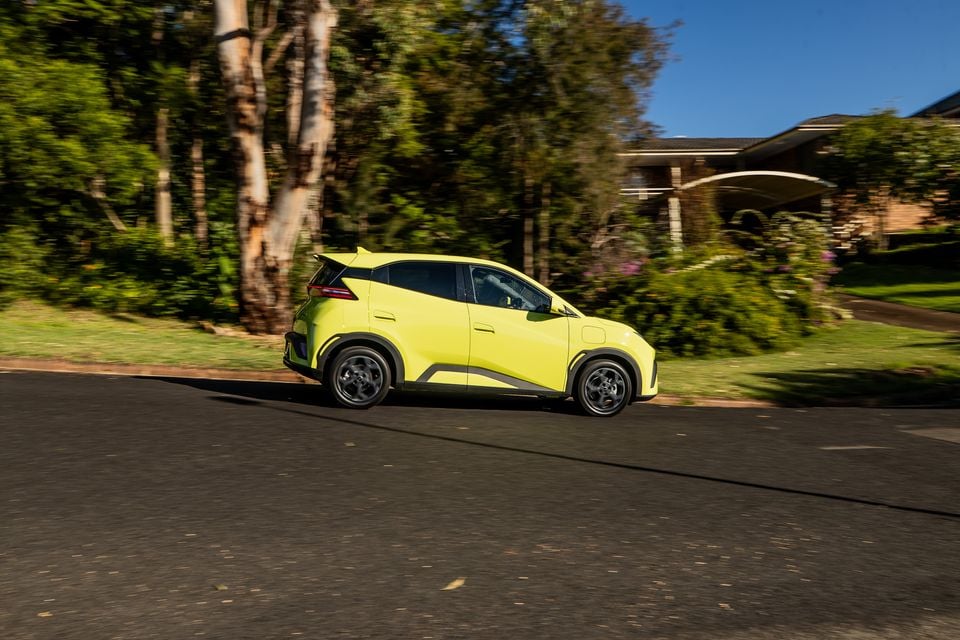 A lime green BYD Atto 1 small SUV driving through a suburban street, seen from the side