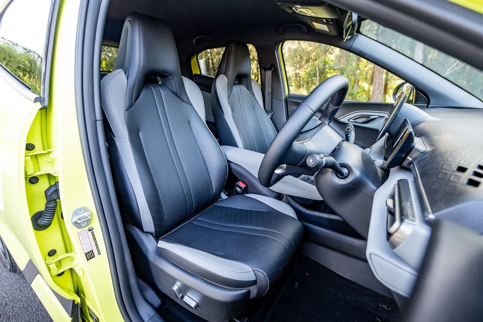Interior view of a 2026 BYD Atto 1 showing the front seats, steering wheel and dashboard, with the driver's door open revealing the yellow exterior