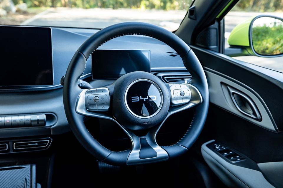 BYD Atto 1 interior showing the leather-wrapped steering wheel with BYD logo, digital instrument cluster, and infotainment screen