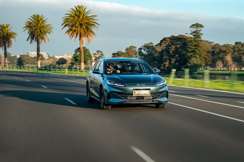 A teal BYD Seal 6 Touring sedan driving on a multi-lane road lined with palm trees in Australia, seen from the front