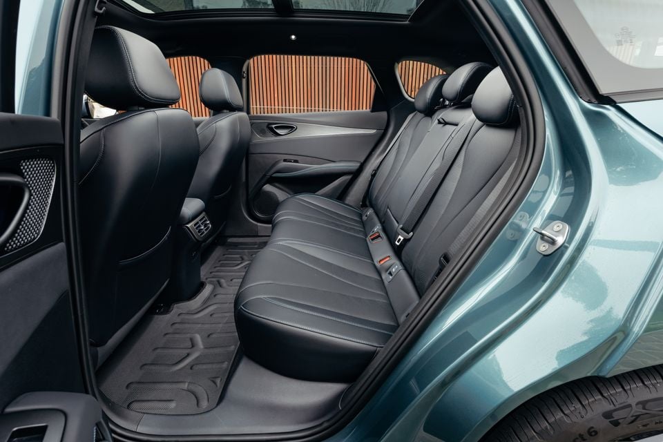 Rear interior of a 2026 BYD Seal 6 Touring showing black leather rear seats with seatbelts, rear air vents, and rubber floor mats, viewed through the open rear door of a teal vehicle