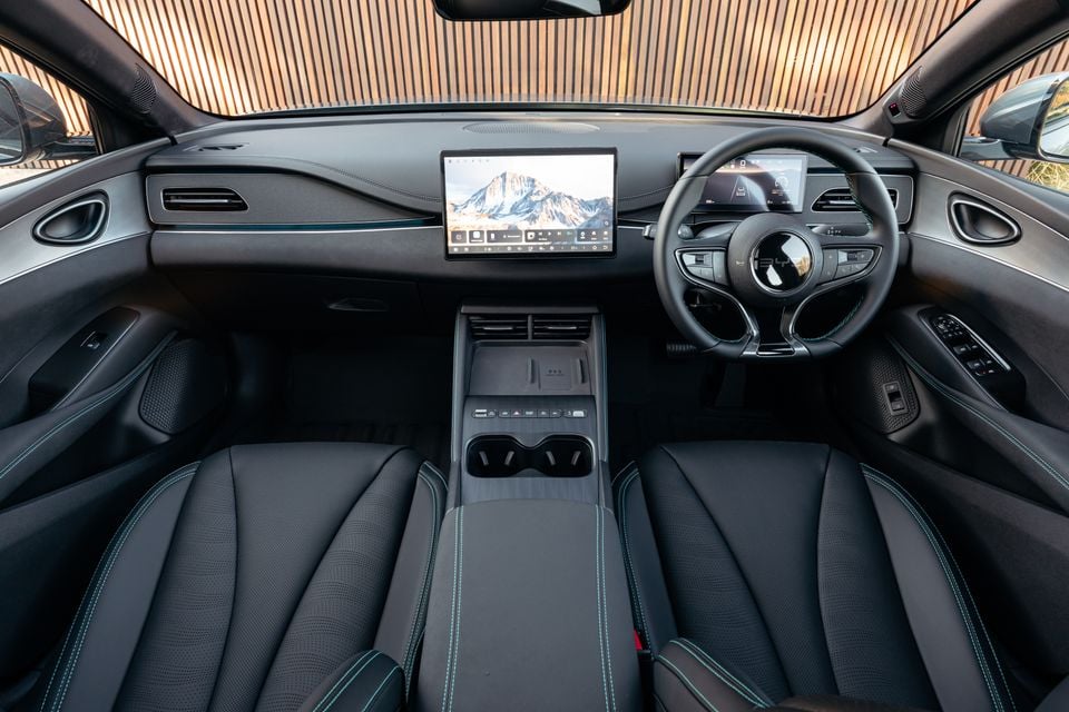 Interior of a 2026 BYD Seal 6 Touring showing the dashboard, large central touchscreen infotainment display, digital instrument cluster, steering wheel, centre console, and front seats with teal stitching, in right-hand drive configuration