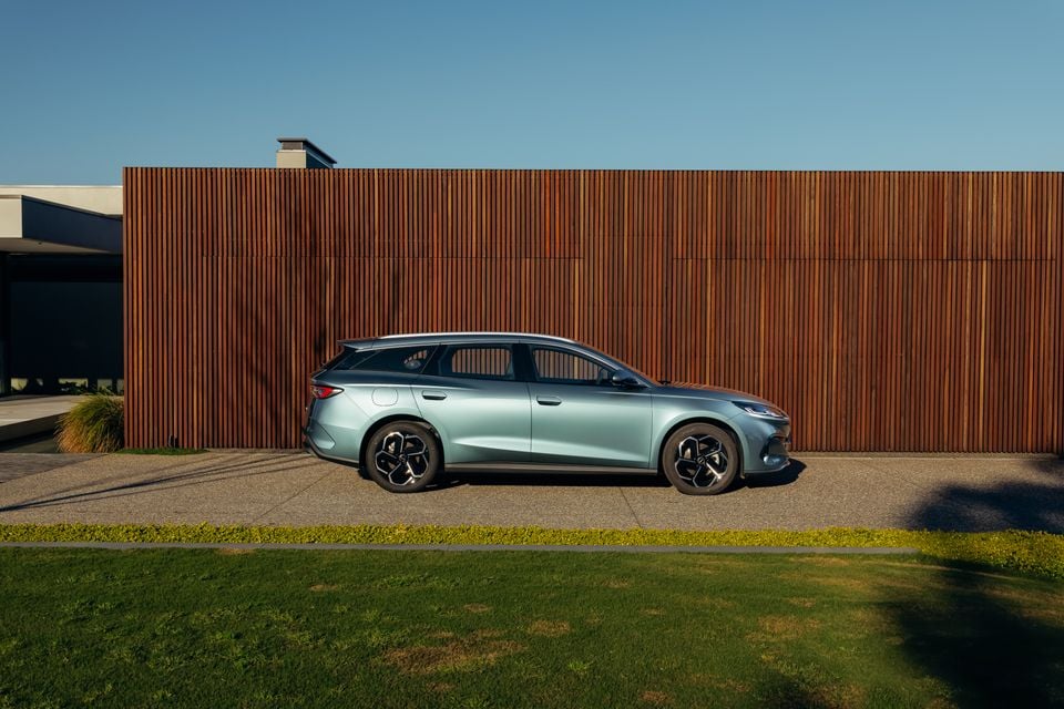 A light blue 2026 BYD Seal 6 Touring wagon seen from the side, parked in front of a timber-clad wall