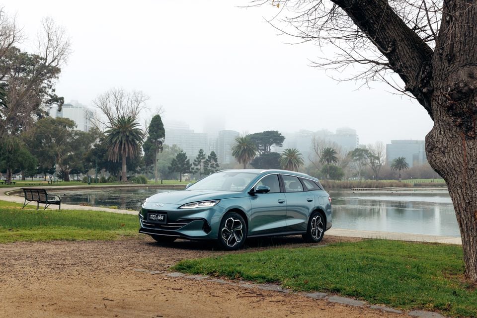 A teal BYD Seal 6 Touring wagon parked beside a lake in a misty park, seen from the front-left side
