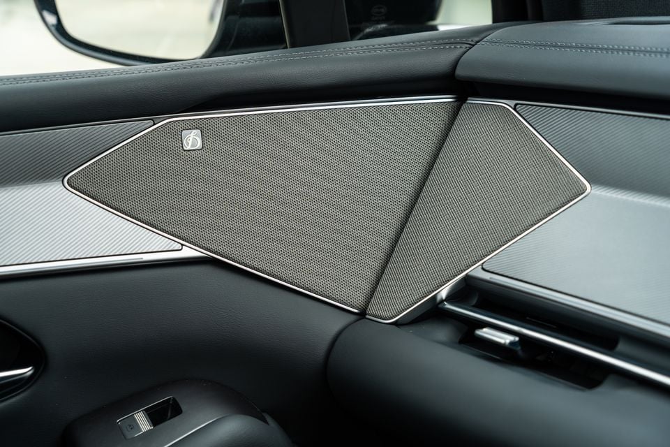 Close-up of a door-mounted speaker grille with chrome trim and a branded badge inside a 2026 BYD Sealion 8, surrounded by dark leather and carbon-fibre-style trim.