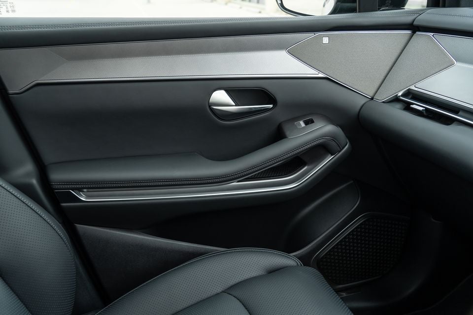 Interior door panel of a 2026 BYD Sealion 8, showing the door trim with a chrome accent strip, door handle, speaker grille, and black leather armrest