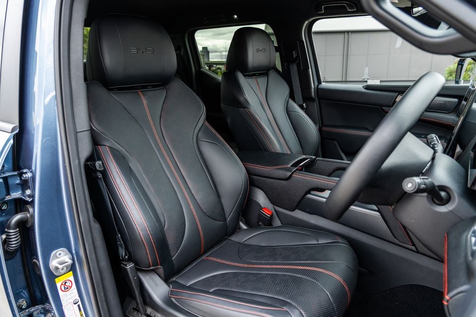 Black leather front seats with red stitching and embossed BYD headrests inside a 2026 BYD Shark 6 Premium, seen through the open passenger door