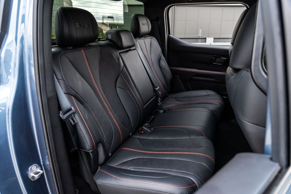 Rear bench seat of a 2026 BYD Shark 6 dual-cab ute in black leather with red contrast stitching and BYD-embossed headrests
