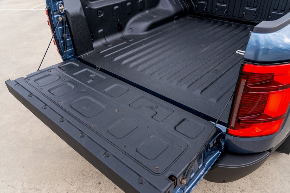 The open tailgate and spray-lined tub of a blue 2026 BYD Shark 6 Premium ute, seen from the rear beside a red tail-light