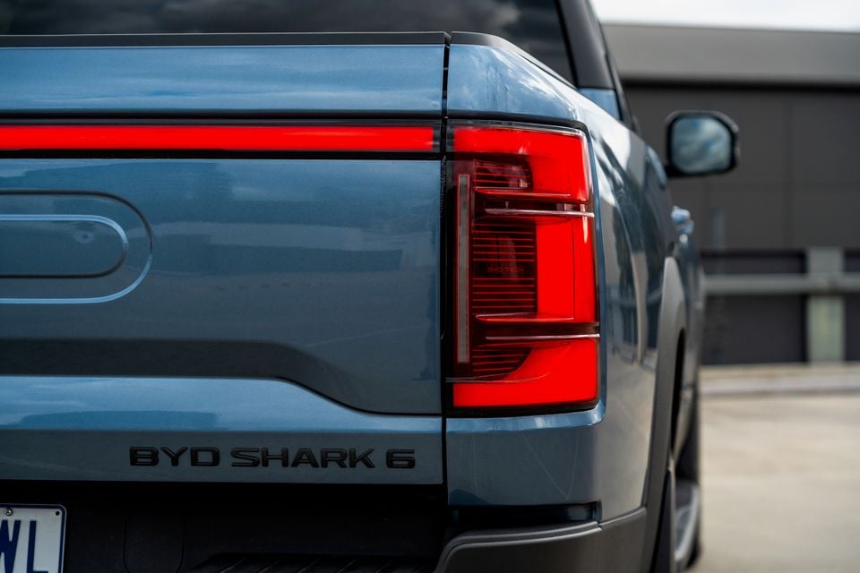 Close-up of the illuminated LED tail-light and tailgate badge on a blue-grey 2026 BYD Shark 6 ute, seen from the rear
