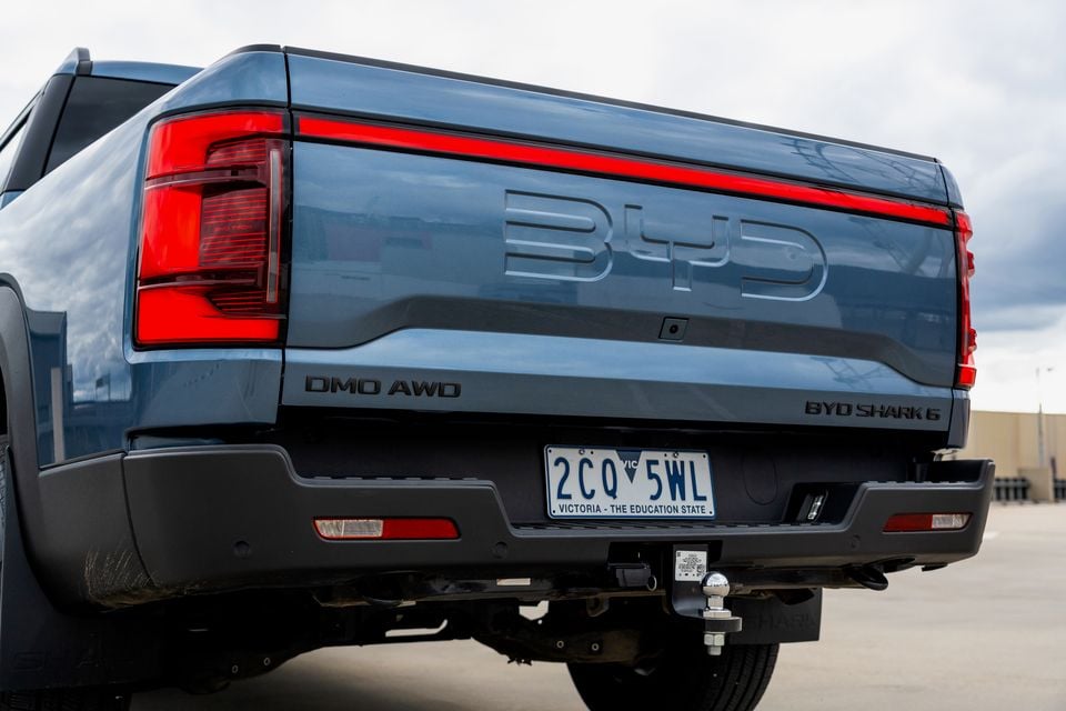 Blue 2026 BYD Shark 6 ute seen from the rear, showing the tailgate with embossed BYD lettering, full-width light bar and tow ball