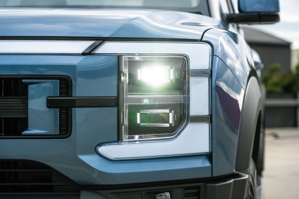 Close-up of the illuminated LED headlight and grille on a light blue 2026 BYD Shark 6 Premium ute