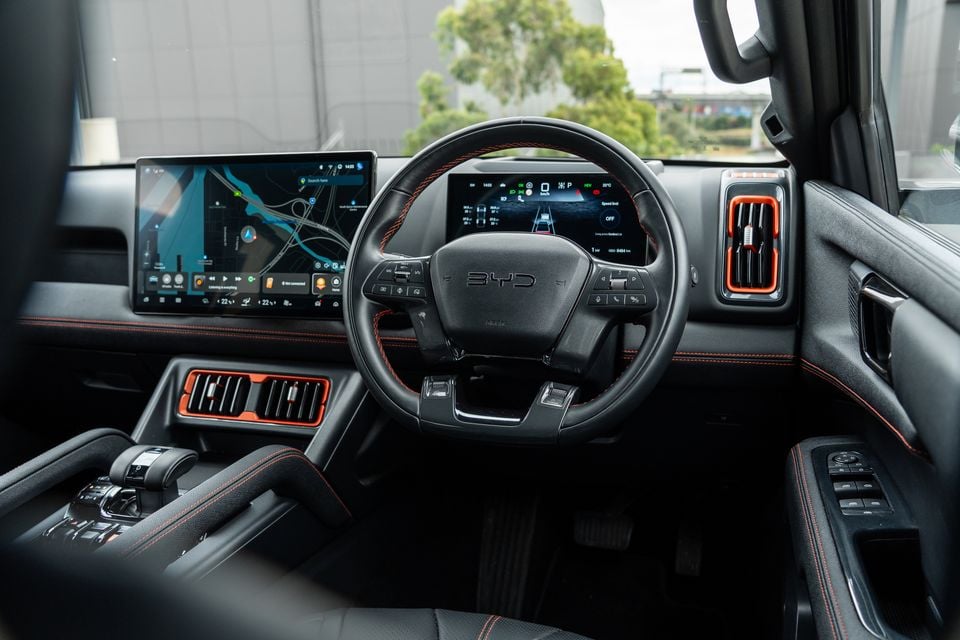 Dashboard of the 2026 BYD Shark 6 Premium ute with steering wheel, digital driver display, central touchscreen showing a map and orange-trimmed air vents