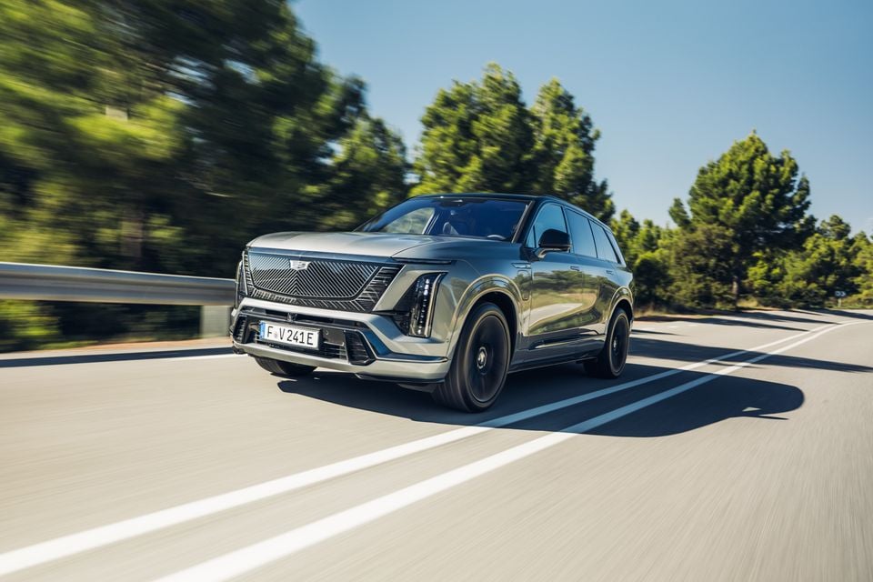 A silver 2026 Cadillac Vistiq large SUV driving on a road, seen from the front-side angle