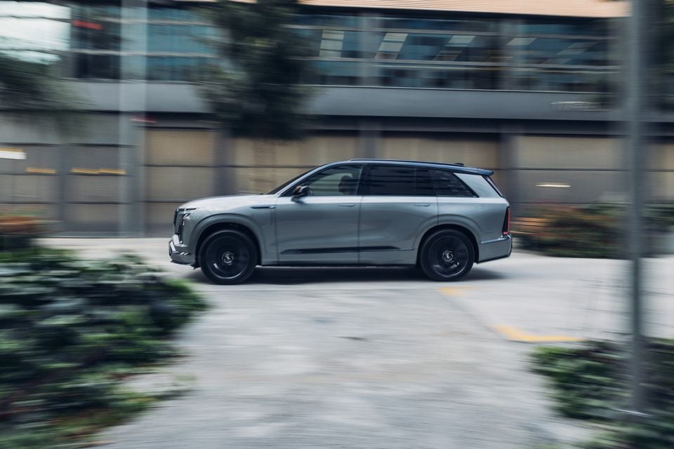 A silver 2026 Cadillac Vistiq large SUV seen from the side while driving through an urban area