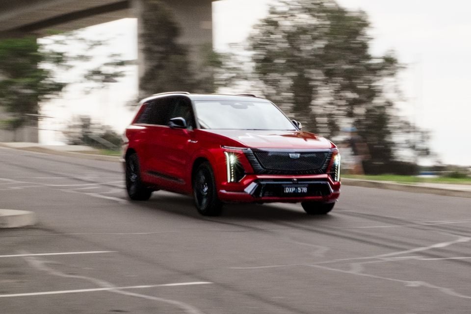 A red 2026 Cadillac VISTIQ Platinum SUV driving through a car park, seen from the front